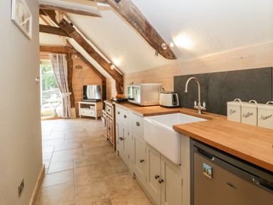 A kitchen with wooden countertops white cabinets a sink toaster microwave and a fridge at The Barn at Rapps Cottage in Rapps near Ilminster