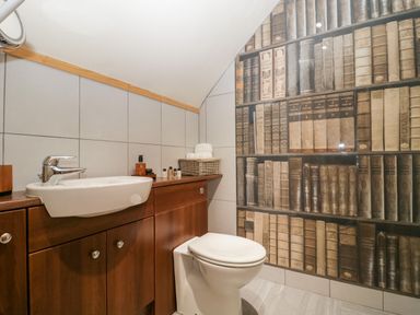 A bathroom with a sink and toilet and a wall decorated with book spines at The Barn at Rapps Cottage in Rapps near Ilminster