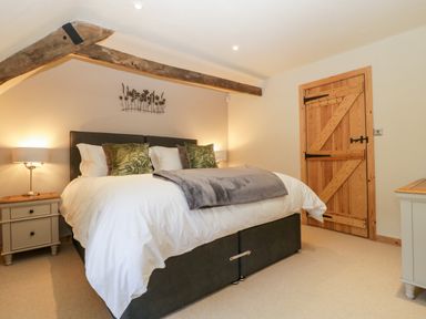 A bedroom with a double bed two bedside tables with lamps a wooden door and exposed wooden beam at The Barn at Rapps Cottage in Rapps near Ilminster
