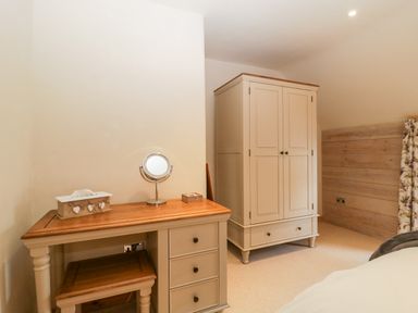 A bedroom with a dressing table mirror wardrobe and floral curtain at The Barn at Rapps Cottage in Rapps near Ilminster