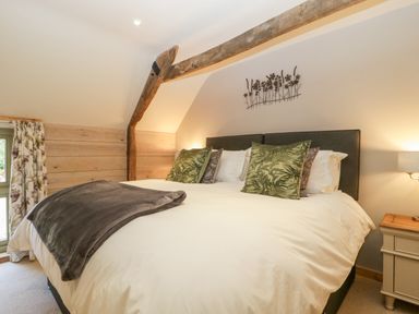 A bedroom with a large bed green cushions wooden beam and bedside table with lamp at The Barn at Rapps Cottage Rapps near Ilminster