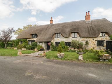 A stone cottage with a thatched roof surrounded by a garden and a paved path at The Barn at Rapps Cottage in Rapps near Ilminster
