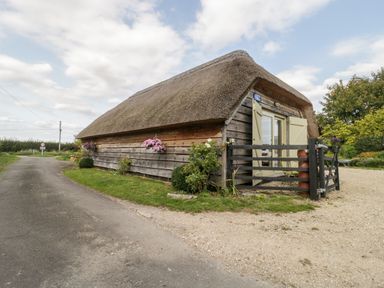 A thatched cottage with wooden siding and flower baskets near a road at The Barn at Rapps Cottage in Rapps near Ilminster