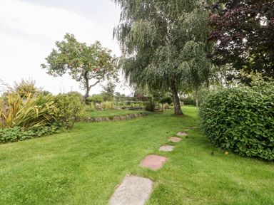 A garden with trees bushes and a stone pathway at The Barn at Rapps Cottage in Rapps near Ilminster