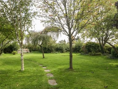 A garden with grass a stone pathway and several trees at The Barn at Rapps Cottage Rapps near Ilminster