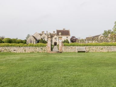 A large stone house behind a stone wall with two pillars and a bench on a lawn at The Barn at Rapps Cottage in Rapps near Ilminster