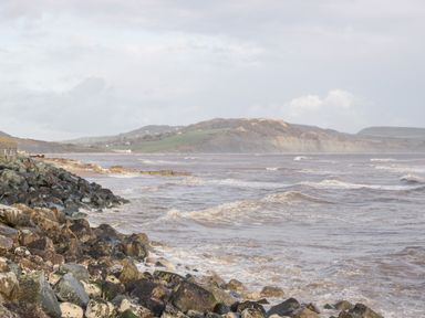 A rocky coastline with waves and hills in the background at The Barn at Rapps Cottage in Rapps near Ilminster