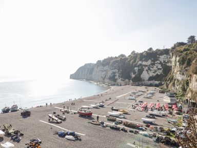 A pebble beach with small boats and red umbrellas near cliffs at The Barn at Rapps Cottage Rapps near Ilminster