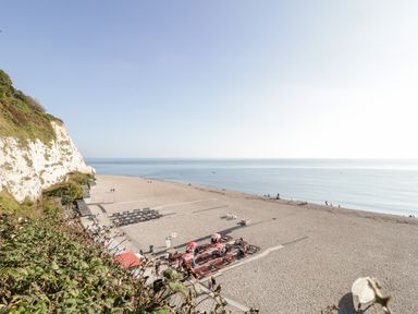 A pebble beach with picnic tables and cliffs by the sea at The Barn at Rapps Cottage in Rapps near Ilminster