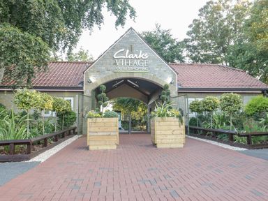 An entrance archway with Clarks Village outlet shopping sign and two wooden planters with plants at The Barn at Rapps Cottage in Rapps near Ilminster