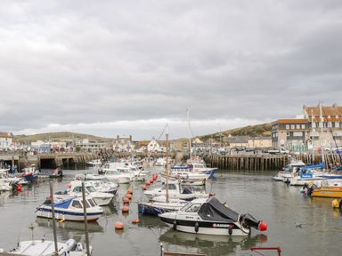 A small harbor with multiple moored boats and buildings along the waterfront at The Barn at Rapps Cottage in Rapps near Ilminster