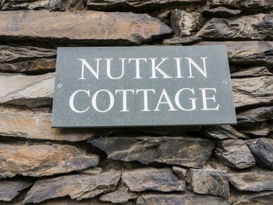 A stone wall with a rectangular sign reading Nutkin Cottage at Nutkin Cottage in Bowness-On-Windermere