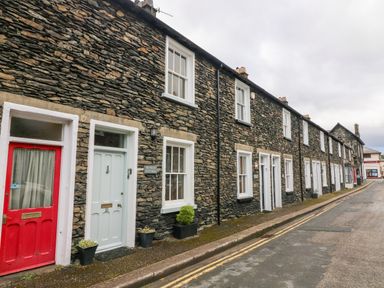 A row of stone cottages with white framed windows and different colored doors along a narrow street at Nutkin Cottage in Bowness-On-Windermere