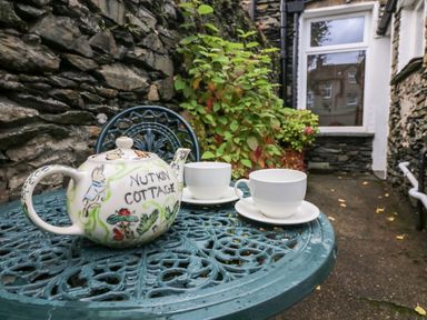 A metal outdoor table with a teapot and two teacups in a stone-walled courtyard at Nutkin Cottage in Bowness-On-Windermere