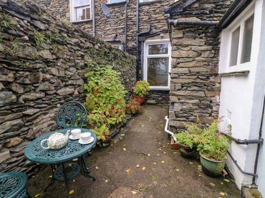 An outdoor stone patio with a table tea set plants and stone walls at Nutkin Cottage Bowness-On-Windermere
