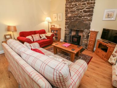 A sitting room with sofas coffee table stone fireplace and television at Nutkin Cottage in Bowness-On-Windermere