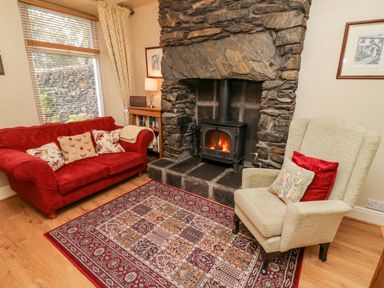 A living room with a stone fireplace a red sofa and an armchair at Nutkin Cottage in Bowness-On-Windermere