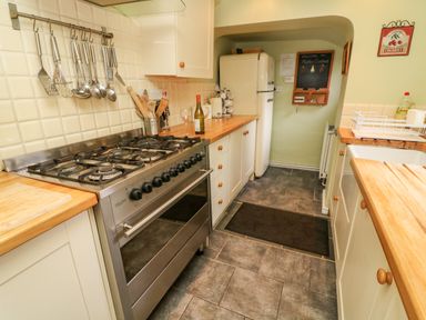 A kitchen with a gas stove refrigerator utensils hanging on a rack and wooden countertops at Nutkin Cottage in Bowness-On-Windermere