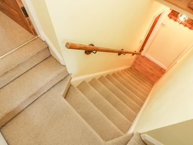 A carpeted staircase with a wooden handrail leading to a hallway with wooden flooring at Nutkin Cottage in Bowness-On-Windermere