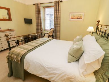 A bedroom with a double bed a chair a window a dresser and a wall-mounted tv at Nutkin Cottage in Bowness-On-Windermere