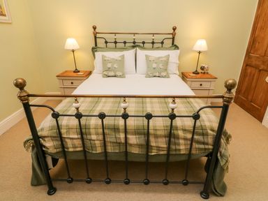 A bedroom with a metal bed frame a white bedspread green plaid blanket two sheep patterned pillows and bedside tables with lamps at Nutkin Cottage in Bowness-On-Windermere