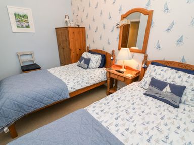 A bedroom with two single beds a wooden wardrobe a bedside table with a lamp and a mirror at Nutkin Cottage in Bowness-On-Windermere