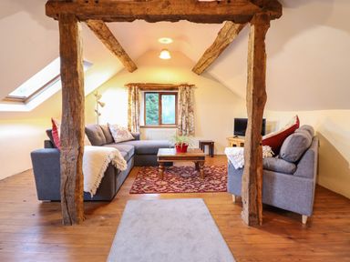 A living room with wooden beams a gray sectional sofa a wooden coffee table and a television at Yr Hen Felin in Llanfyllin