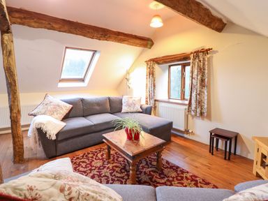 A living room with a gray sectional sofa wooden coffee table and floral curtains at Yr Hen Felin in Llanfyllin