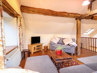 A living room with wooden beams a gray sofa a wooden coffee table with a plant and a television at Yr Hen Felin in Llanfyllin