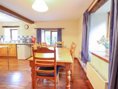 A kitchen and dining area with a wooden table and chairs next to windows with curtains at Yr Hen Felin in Llanfyllin