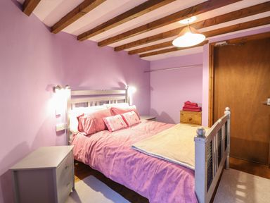 A bedroom with a double bed pink bedding a wooden chest of drawers and exposed wooden ceiling beams at Yr Hen Felin Llanfyllin