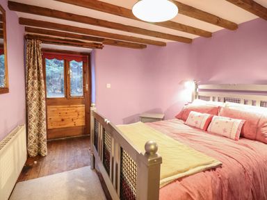 A bedroom with a bed covered in pink bedding next to a wooden door and floral curtain at Yr Hen Felin in Llanfyllin