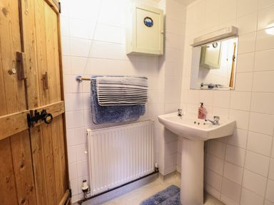 A bathroom with a pedestal sink a mirror towels on a rack and a wooden door at Yr Hen Felin in Llanfyllin