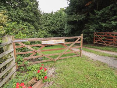 A wooden gate with a sign reading Yr Hen Felin beside a gravel driveway and trees at Yr Hen Felin in Llanfyllin