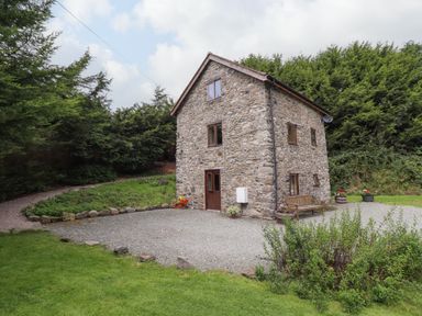 A stone house with wooden windows and doors surrounded by gravel and greenery at Yr Hen Felin in Llanfyllin