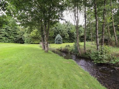 A grassy area with trees a small stream and bushes at Yr Hen Felin in Llanfyllin