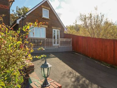 A driveway with a brick house with balcony and a red wooden fence at Ffau'r Ddraig in Cross Hands