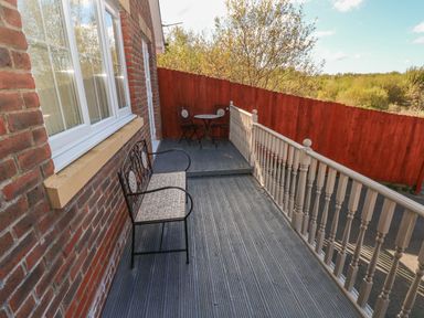An outdoor deck with a bench and a small round table with two chairs by a red wooden fence at Ffau'r Ddraig in Cross Hands