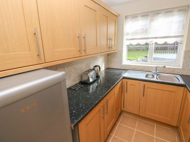 A kitchen with wooden cabinets black countertop a toaster electric kettle a sink and a window at Ffau'r Ddraig in Cross Hands