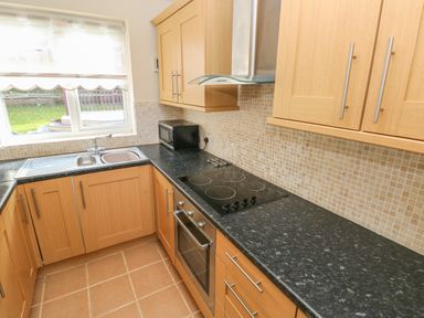 A kitchen with wooden cabinets a black countertop an electric stove an oven a microwave and a double sink under a window at Ffau'r Ddraig in Cross Hands