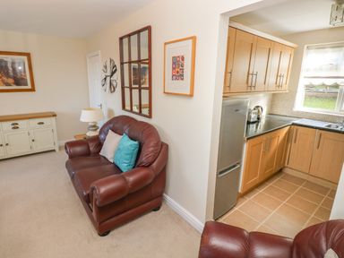 A living room with a brown leather sofa and a lamp next to a kitchen with wooden cabinets at Ffau'r Ddraig in Cross Hands