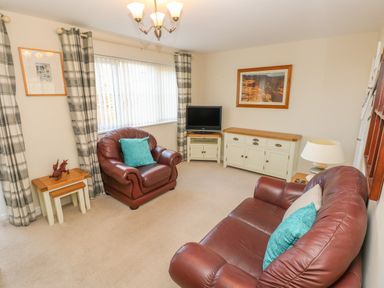A living room with two brown leather sofas a television on a white stand a wooden sideboard a lamp and framed pictures at Ffau'r Ddraig in Cross Hands