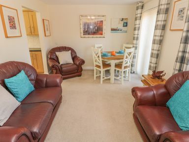 A living room with brown leather sofas a wooden dining table with four chairs and wall art at Ffau'r Ddraig in Cross Hands