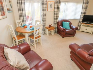 A living room with a round dining table set for four and three brown leather armchairs at Ffau'r Ddraig in Cross Hands