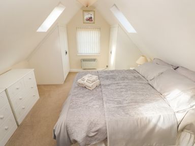 A bedroom with a bed centered under a sloped ceiling with two skylights white wardrobes on either side and a dresser on the left at Ffau'r Ddraig in Cross Hands