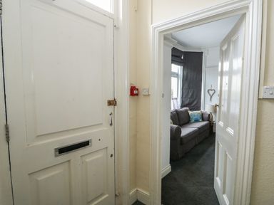 A hallway with a white door and an open door leading to a living room with a gray sofa and cushions at Northgate Ground Floor Flat in Hunstanton