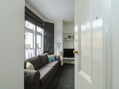 A living room with a dark sofa pillows a lamp a television and window blinds at Northgate Ground Floor Flat in Hunstanton