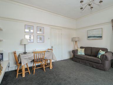 A living room with a sofa and pillows next to a dining table with chairs and lamps at Northgate Ground Floor Flat in Hunstanton