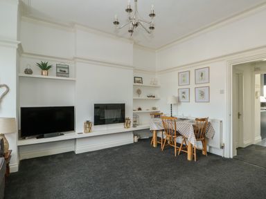 A living room with a wall mounted television and fireplace a dining table with four chairs and framed pictures on the wall at Northgate Ground Floor Flat in Hunstanton