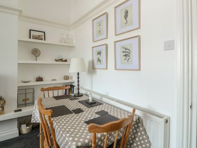 A dining table with polka dot tablecloth and wooden chairs by a wall with framed sea creature pictures and shelves with decorative items at Northgate Ground Floor Flat in Hunstanton